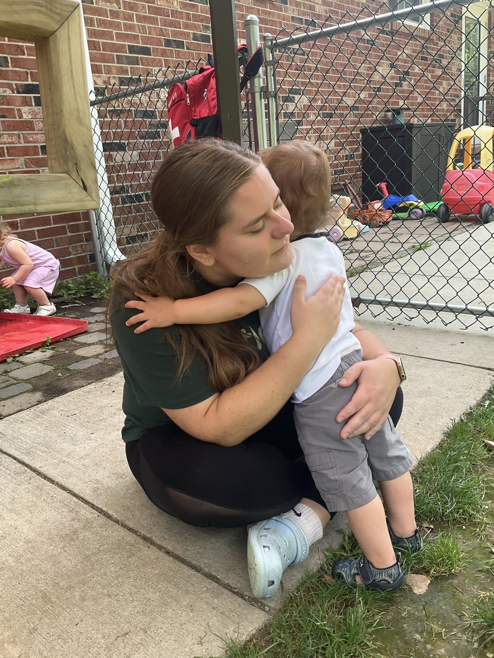 Little Acorns teacher hugging a child outside — primary caregiving builds trusting relationships