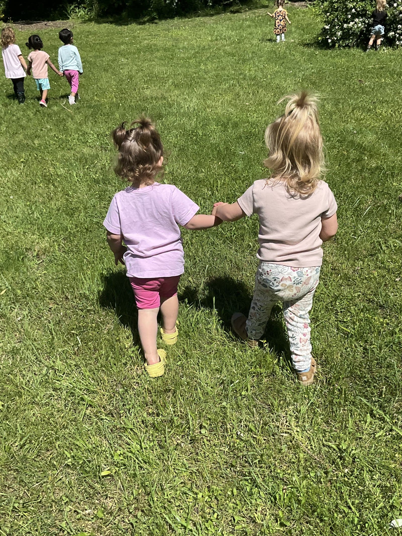 Little Acorns saplings classroom — toddlers walking together outside in the sunshine