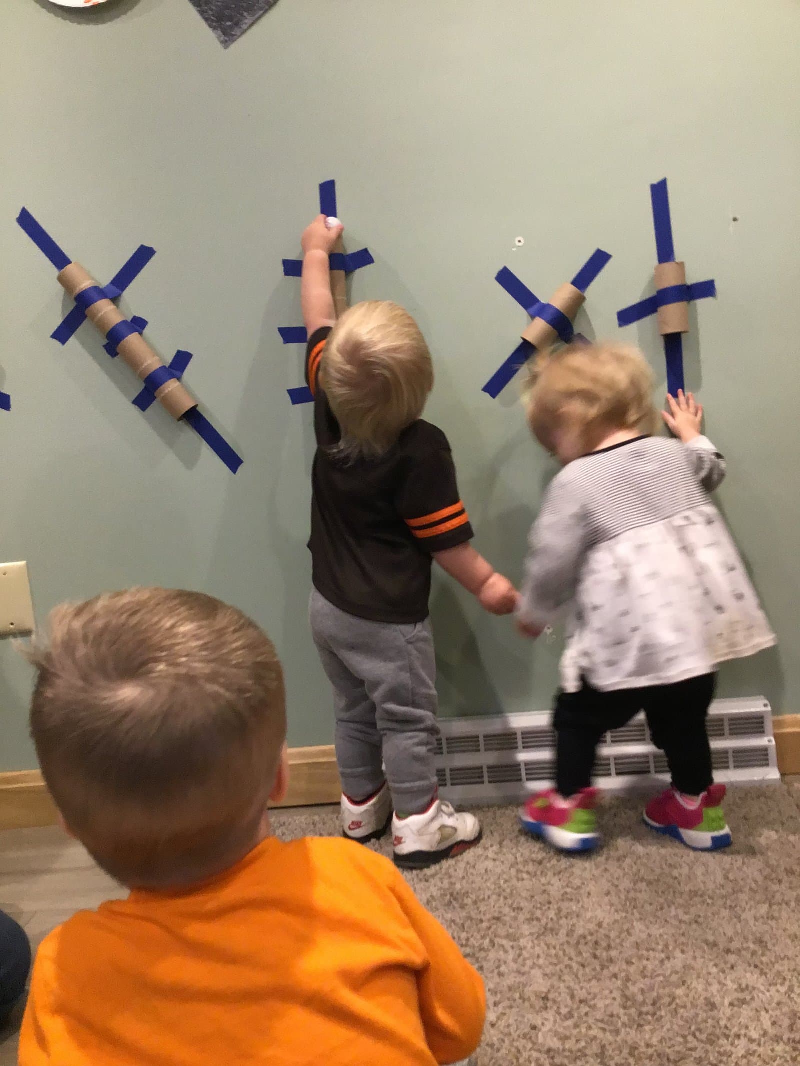 Little Acorns Sprouts toddlers exploring a tape-and-tube wall art project in their classroom
